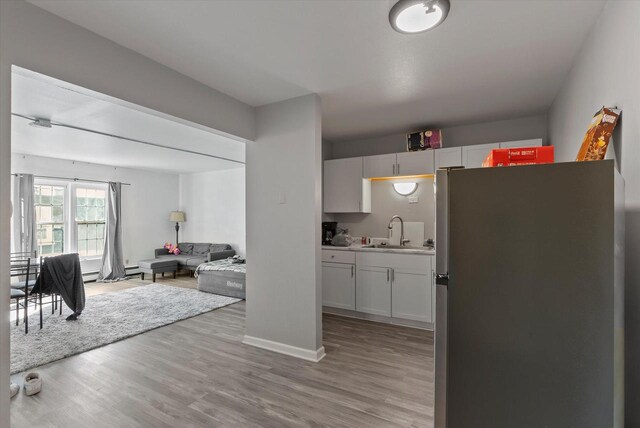 kitchen featuring stainless steel fridge, white cabinetry, sink, and light hardwood / wood-style flooring