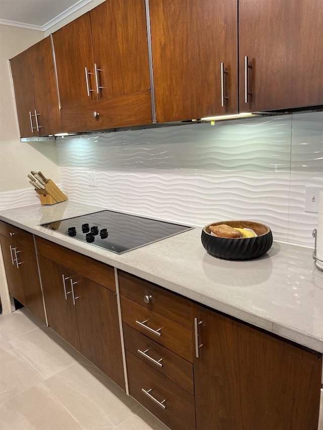 kitchen with light stone counters, ornamental molding, light tile patterned floors, backsplash, and black electric cooktop