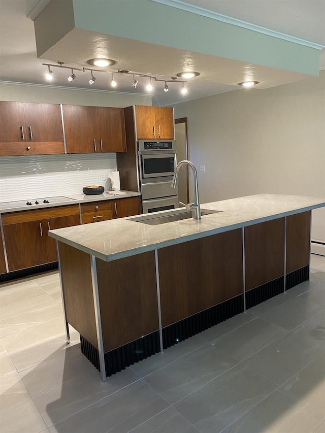 kitchen featuring light tile patterned flooring, sink, backsplash, double oven, and an island with sink