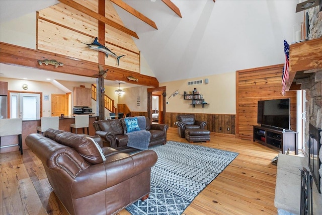 living room with wooden walls, high vaulted ceiling, light wood-type flooring, and beamed ceiling