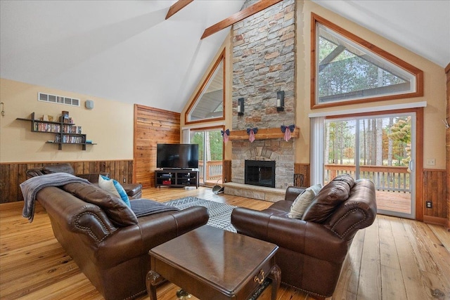 living room with light hardwood / wood-style floors, high vaulted ceiling, wooden walls, and a stone fireplace