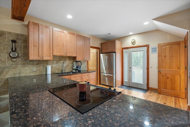 kitchen with light hardwood / wood-style floors, tasteful backsplash, dark stone countertops, sink, and black appliances