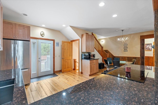 kitchen with lofted ceiling, stainless steel refrigerator, a notable chandelier, hanging light fixtures, and light hardwood / wood-style flooring