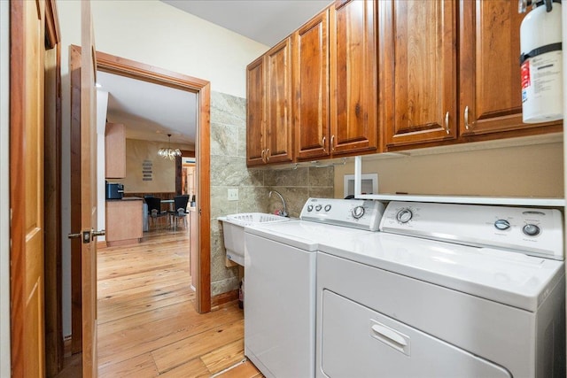 laundry room with light wood-type flooring, sink, an inviting chandelier, cabinets, and washing machine and dryer