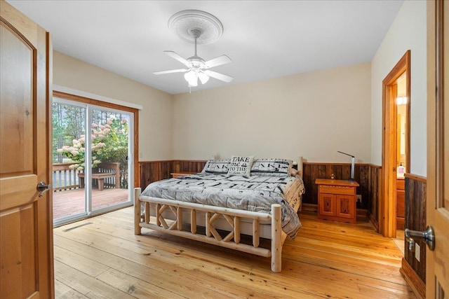 bedroom featuring wood walls, light hardwood / wood-style floors, access to exterior, and ceiling fan