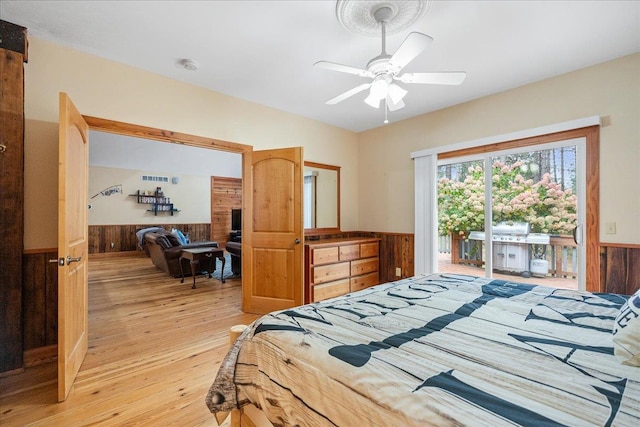 bedroom featuring ceiling fan, wood walls, light hardwood / wood-style floors, and access to outside