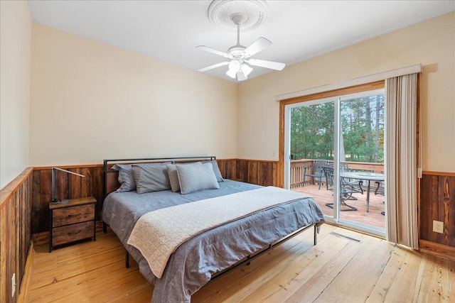 bedroom featuring wood walls, access to exterior, light hardwood / wood-style flooring, and ceiling fan