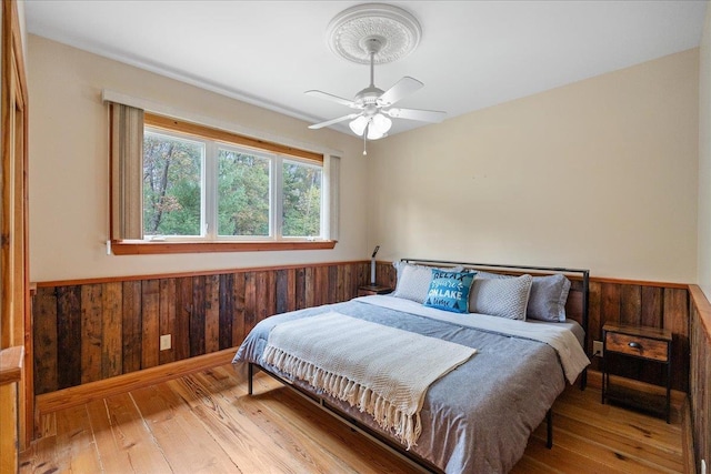 bedroom with ceiling fan, wooden walls, and light wood-type flooring