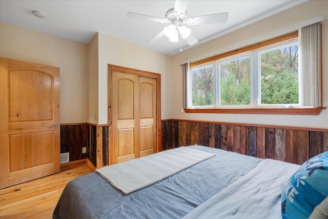 bedroom featuring wood walls, wood-type flooring, a closet, and ceiling fan