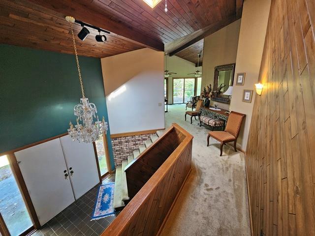 corridor featuring carpet floors, vaulted ceiling with beams, an inviting chandelier, and wood ceiling