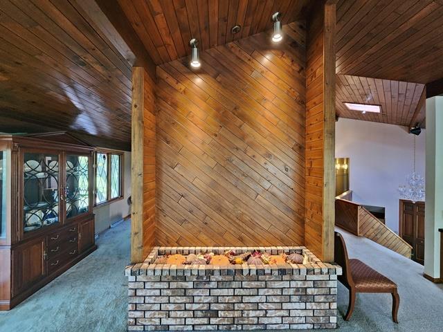 interior space with a skylight, carpet flooring, wooden ceiling, wooden walls, and high vaulted ceiling