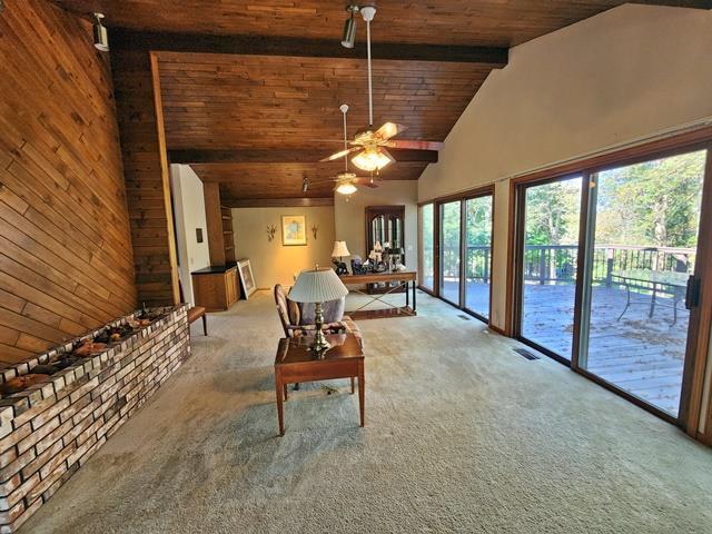 unfurnished living room featuring high vaulted ceiling, beamed ceiling, ceiling fan, wooden ceiling, and carpet floors