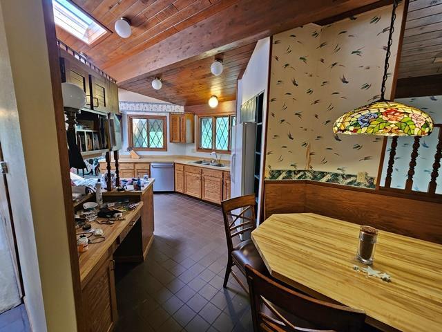 kitchen with pendant lighting, dark tile patterned flooring, dishwasher, lofted ceiling with skylight, and wooden ceiling