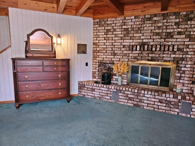 unfurnished living room with a fireplace, beam ceiling, carpet, and wooden walls