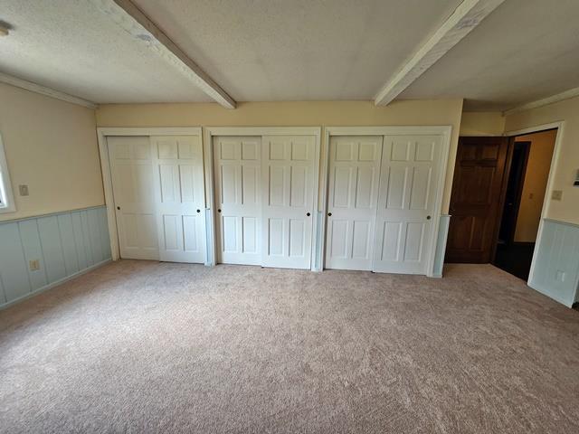 unfurnished bedroom with light carpet, beamed ceiling, a textured ceiling, and two closets