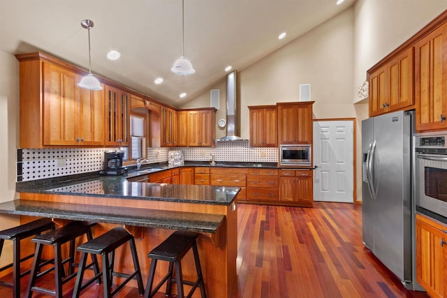 kitchen with hanging light fixtures, wall chimney range hood, stainless steel appliances, a breakfast bar area, and dark hardwood / wood-style flooring