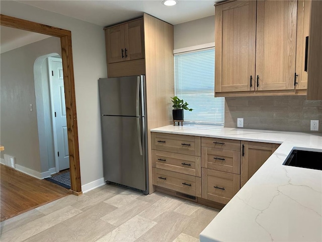 kitchen with tasteful backsplash, stainless steel fridge, light hardwood / wood-style flooring, and light stone counters