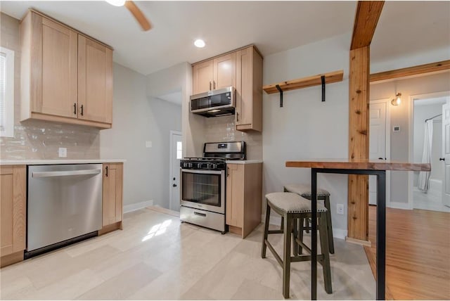 kitchen featuring ceiling fan, light brown cabinets, stainless steel appliances, decorative backsplash, and light wood-type flooring