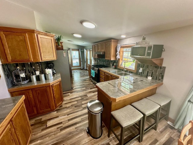 kitchen with appliances with stainless steel finishes, kitchen peninsula, light hardwood / wood-style floors, and backsplash