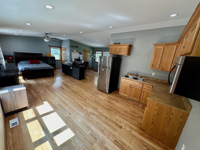 kitchen with stainless steel fridge, sink, light wood-type flooring, and vaulted ceiling