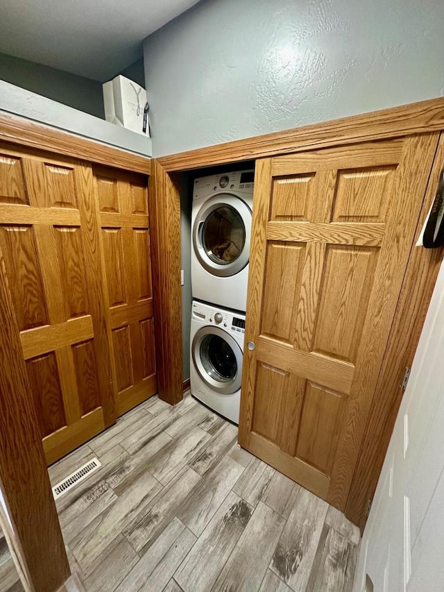 laundry area with light hardwood / wood-style floors and stacked washer and clothes dryer