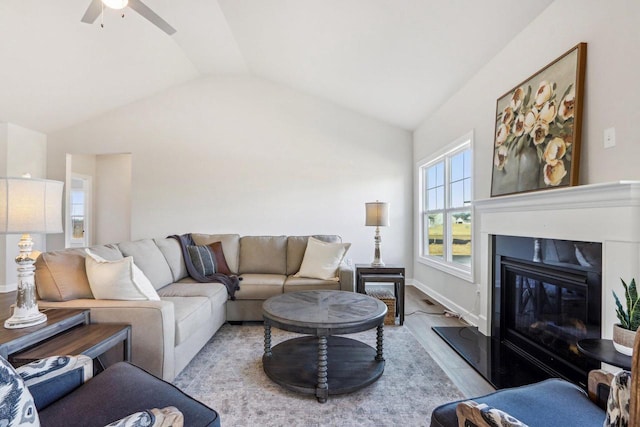 living area featuring baseboards, a ceiling fan, a glass covered fireplace, wood finished floors, and vaulted ceiling