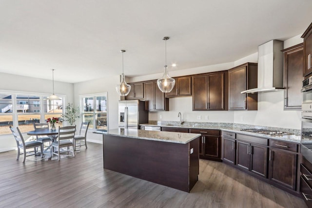 kitchen featuring dark wood-style floors, appliances with stainless steel finishes, a sink, wall chimney range hood, and dark brown cabinetry