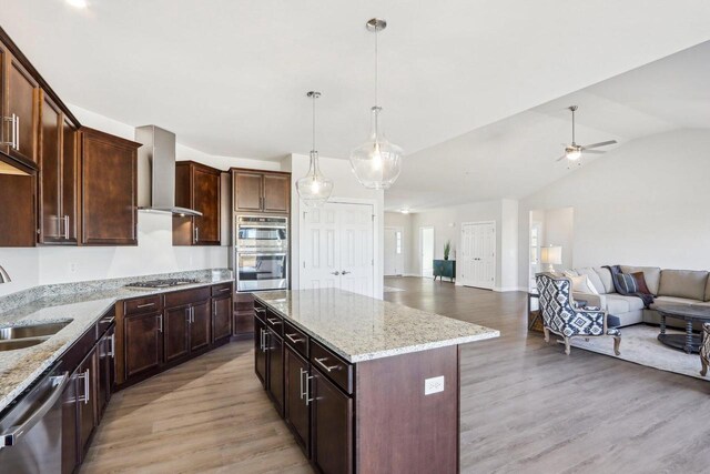 kitchen featuring a sink, light wood-style floors, open floor plan, wall chimney range hood, and appliances with stainless steel finishes