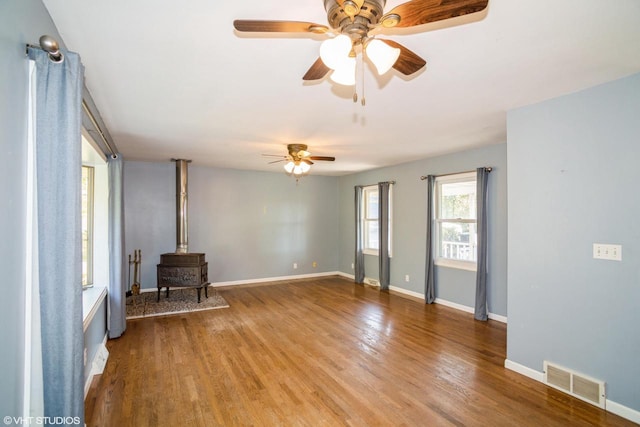 unfurnished living room featuring a wood stove, hardwood / wood-style flooring, and ceiling fan