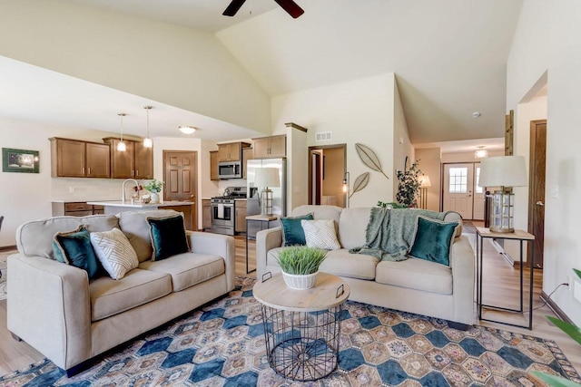 living room with ceiling fan, sink, light hardwood / wood-style floors, and high vaulted ceiling