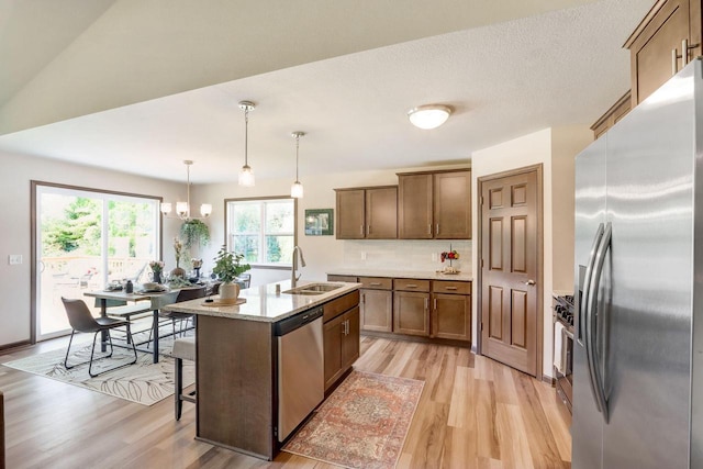 kitchen with hanging light fixtures, sink, a kitchen island with sink, light hardwood / wood-style flooring, and stainless steel appliances