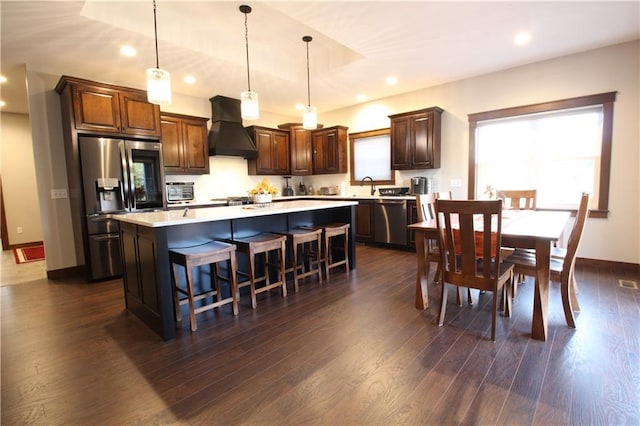 kitchen with dark hardwood / wood-style flooring, custom range hood, hanging light fixtures, appliances with stainless steel finishes, and a center island