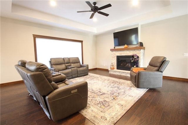 living room featuring dark wood-type flooring, a stone fireplace, and a raised ceiling