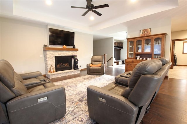 living room with a fireplace, ceiling fan, dark wood-type flooring, and a raised ceiling