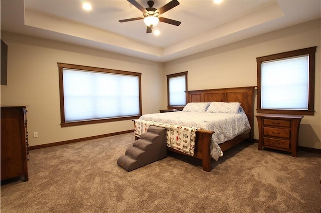 carpeted bedroom featuring ceiling fan, multiple windows, and a tray ceiling