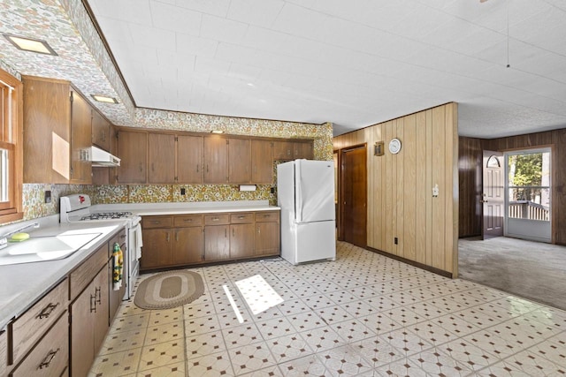 kitchen featuring white appliances, sink, wooden walls, and light carpet