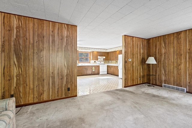 unfurnished living room featuring wooden walls and light carpet