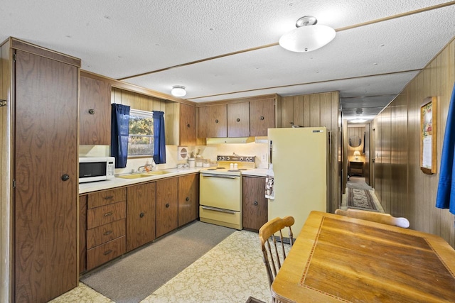 kitchen with sink, white appliances, wooden walls, range hood, and light carpet