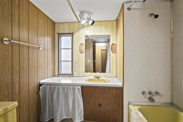 bathroom featuring shower / tub combination, vanity, wood walls, and a textured ceiling