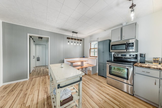 kitchen with stainless steel appliances, hanging light fixtures, gray cabinetry, and light wood-type flooring