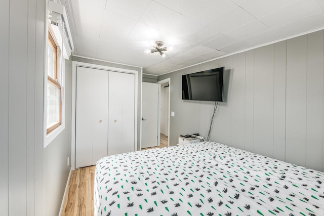 bedroom with wooden walls, a closet, and light hardwood / wood-style flooring