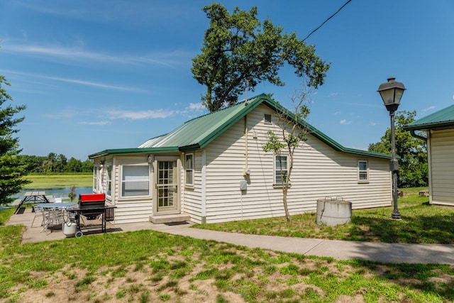 back of house with a water view, a lawn, and a patio area