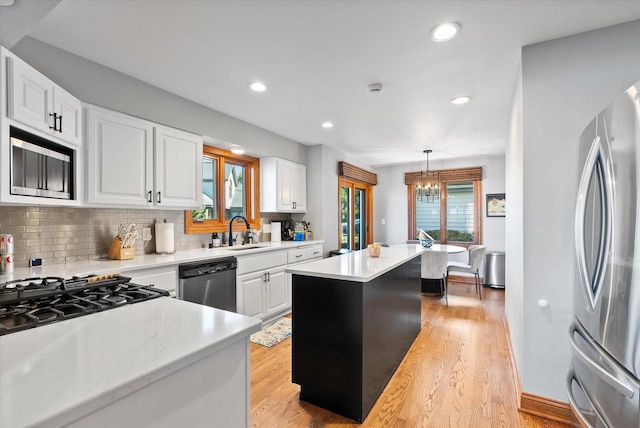 kitchen with a kitchen island, white cabinets, light hardwood / wood-style floors, pendant lighting, and appliances with stainless steel finishes