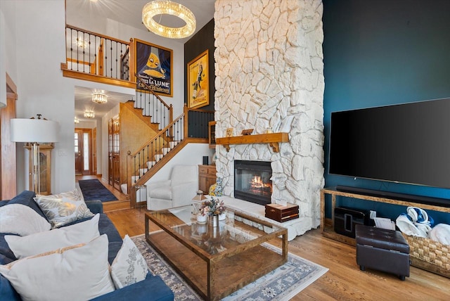 living room with light wood-type flooring, a notable chandelier, a stone fireplace, and a towering ceiling