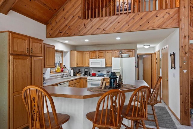 kitchen with kitchen peninsula, sink, white appliances, a breakfast bar, and carpet floors