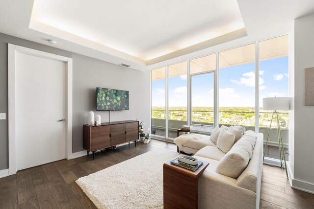 living room featuring floor to ceiling windows, visible vents, a tray ceiling, and dark wood finished floors