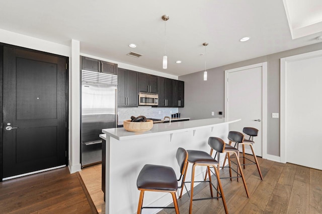 kitchen featuring decorative light fixtures, a kitchen island with sink, dark wood-type flooring, appliances with stainless steel finishes, and a kitchen breakfast bar