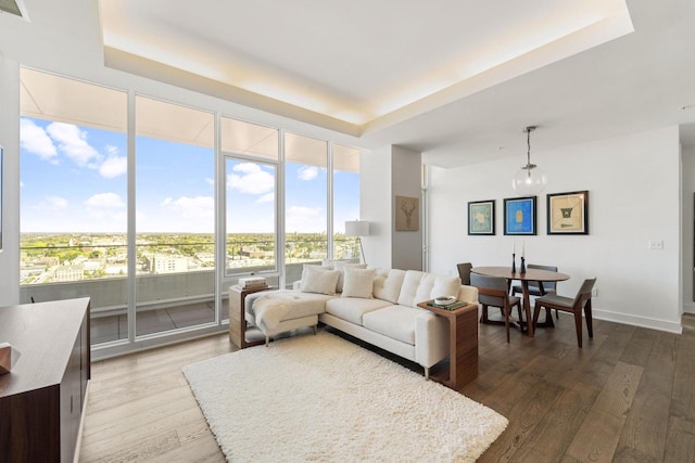 living area with a tray ceiling, wood finished floors, and a wall of windows