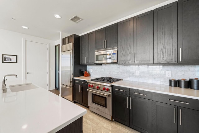 kitchen with light tile patterned floors, premium appliances, sink, and decorative backsplash