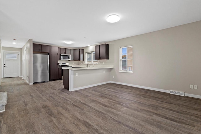 kitchen featuring a breakfast bar, kitchen peninsula, hardwood / wood-style floors, dark brown cabinets, and appliances with stainless steel finishes